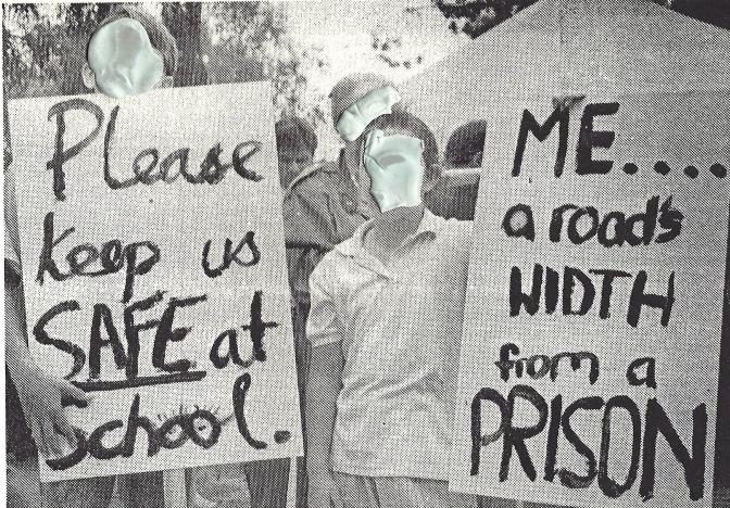 1991 photograph of John XXIII students and parents at a picket, holding hand-lettered signs reading 'Please keep us SAFE at School' and 'ME... a road's WIDTH from a PRISON'.