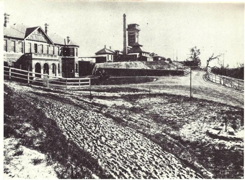 Historical photograph of the approach to Claremont Hospital in 1912, showing the original hospital buildings, a water tower, and an unsealed sandy road with no surrounding development.